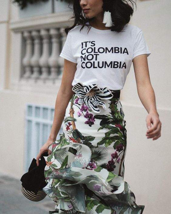 Modelo con una camiseta blanca con las palabras "It's Colombia Not Columbia" en letras negras y una falda de boleros con un patrón floral.